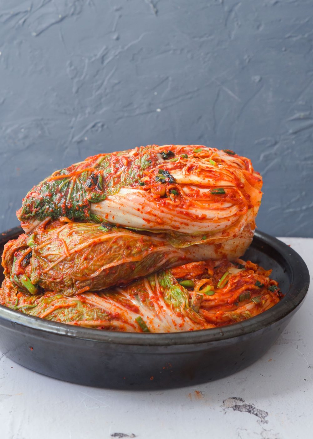 Several whole cabbage kimchi stacked up in a container.