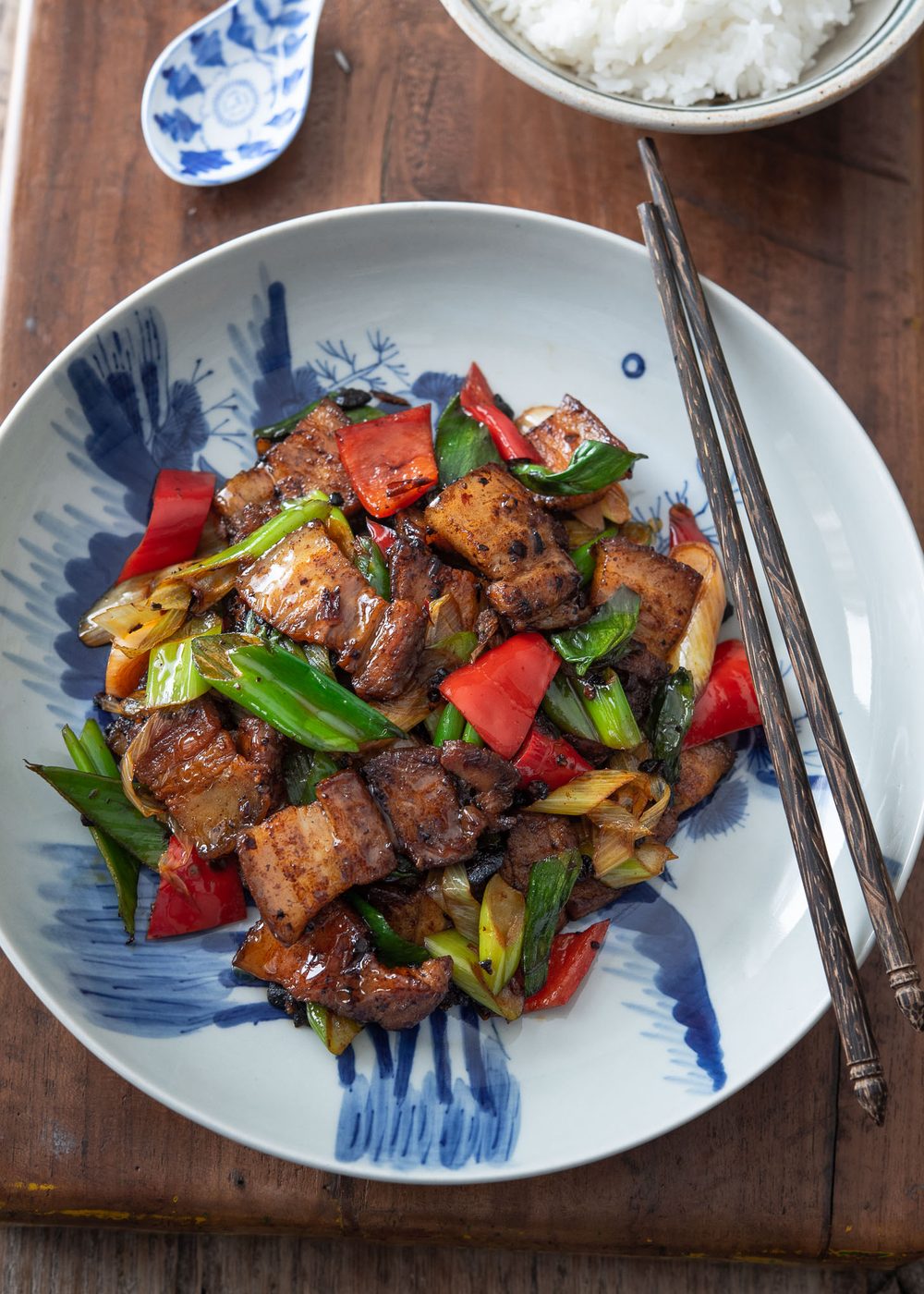 Sichuan twice cooked pork is presented in a blue and white plate with chopsticks.