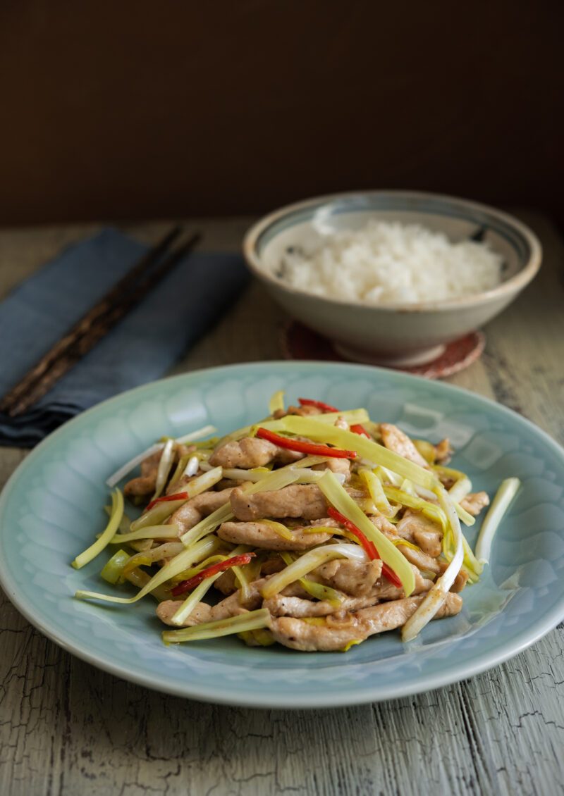 Chicken and yellow chives stir fry on a blue plate is served with a bowl of rice.