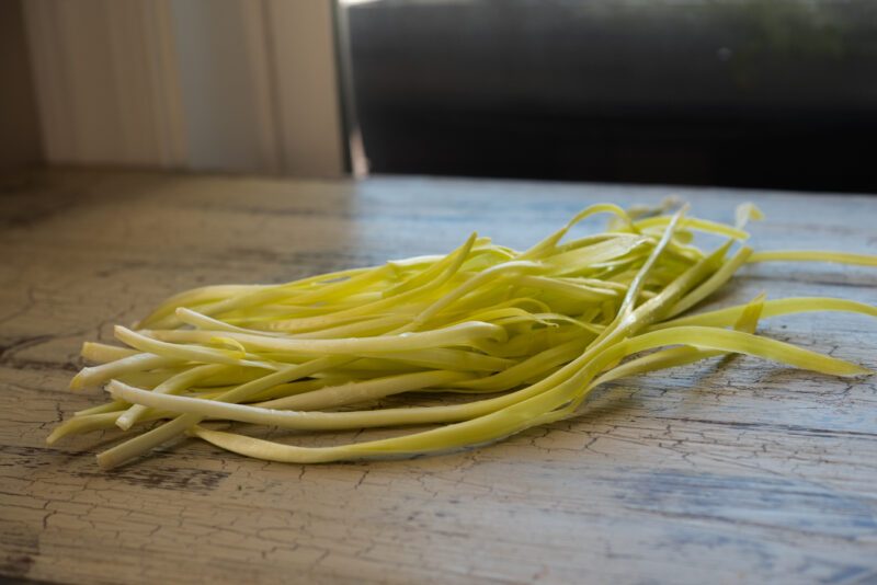 A bunch of Chinese yellow chives are on the wooden surface showing its yellowness.