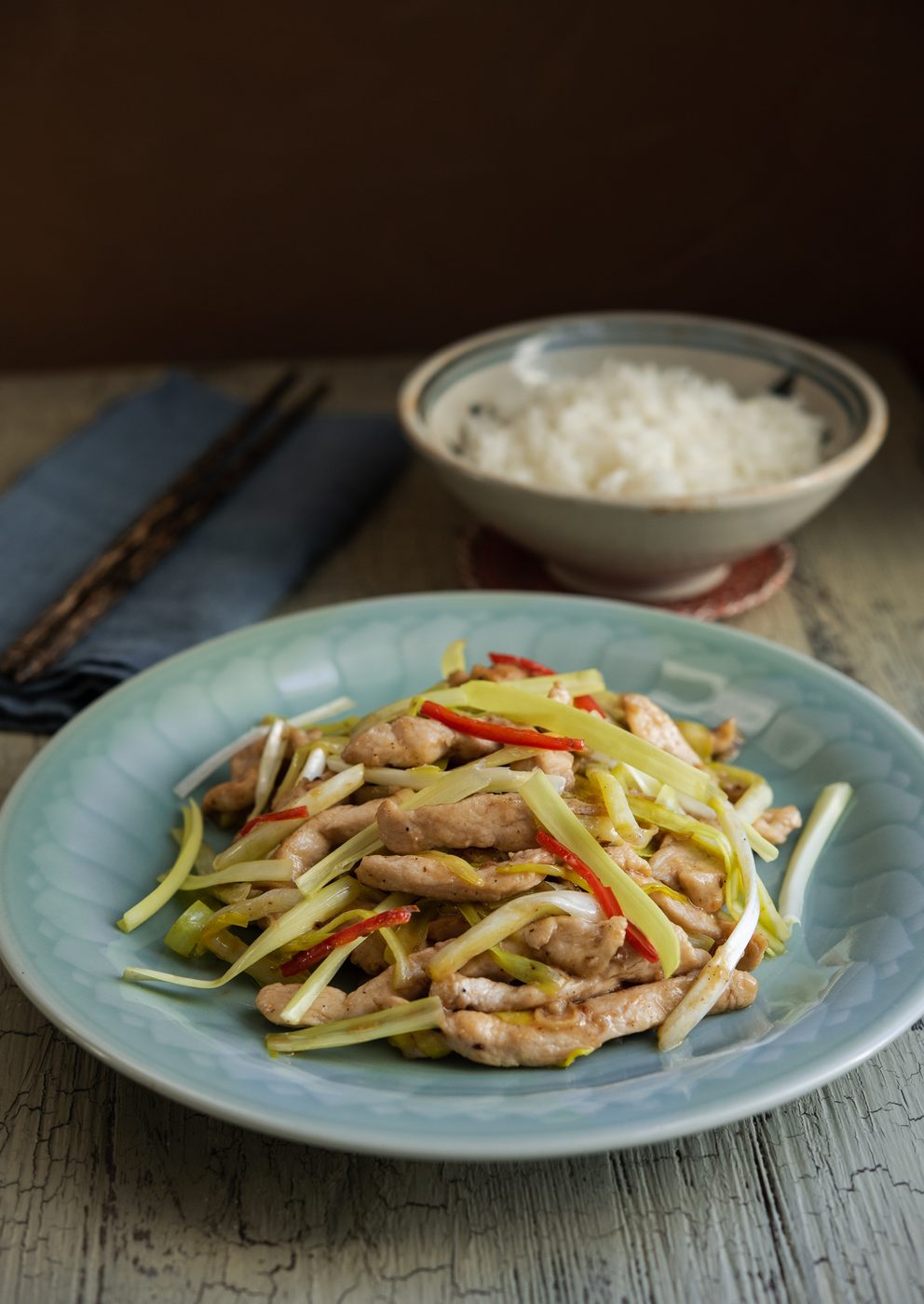 Chicken and yellow chives stir fry on a blue plate is served with a bowl of rice.
