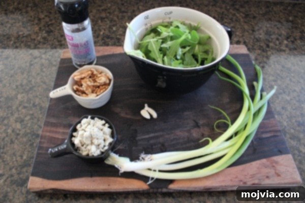 Robust Arugula Walnut Blue Cheese Pesto 4 Fresh ingredients laid out for Arugula Walnut Blue Cheese Pesto: arugula, garlic, walnuts, blue cheese, green onions, and olive oil.