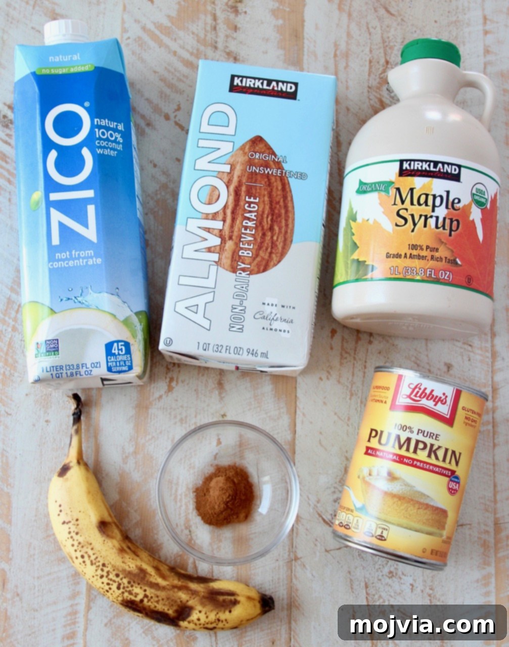 Autumn Glow Smoothie 3 Fresh ingredients laid out for making a superfood pumpkin smoothie: pumpkin puree, banana, almond milk, coconut water, maple syrup, cinnamon, and ice.