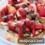 Strawberry Bliss Bites 9 Diced strawberries with fresh basil on a toasted piece of bread, spread with goat cheese, on a plate. Perfect Strawberry Bruschetta.