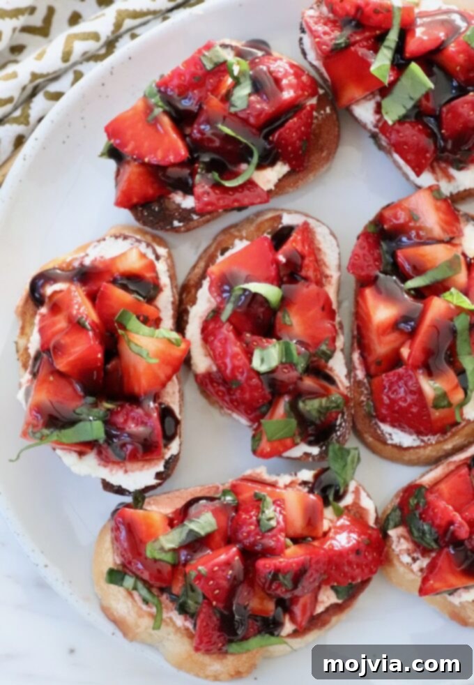 Strawberry Bliss Bites 7 A perfectly assembled Strawberry Bruschetta, featuring toasted baguette, a layer of creamy goat cheese, and a generous topping of diced strawberries and basil, artfully arranged on a plate.