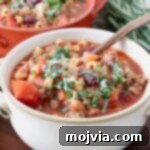 A beautiful white bowl of Pasta Fagioli soup with a copper spoon, highlighting its comforting appeal.