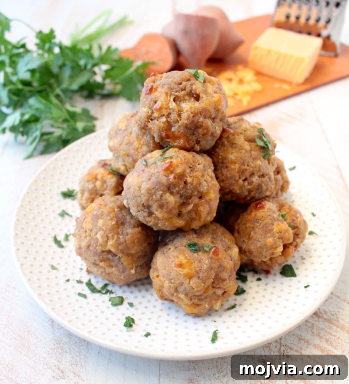 Stacked gluten-free sweet potato sausage balls on a white plate, showcasing their golden-brown exterior and inviting texture.