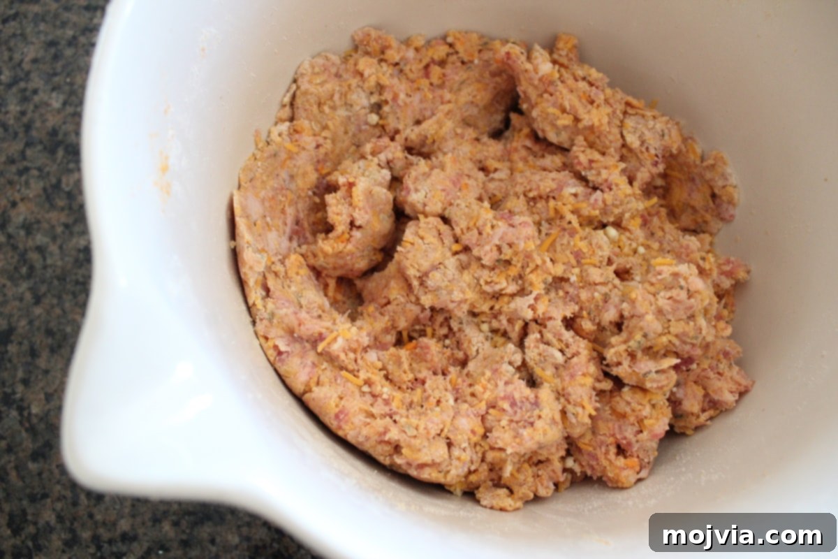 A white bowl holds the well-combined mixture of sweet potato, sausage, cheese, and gluten-free Bisquick, ready for forming.