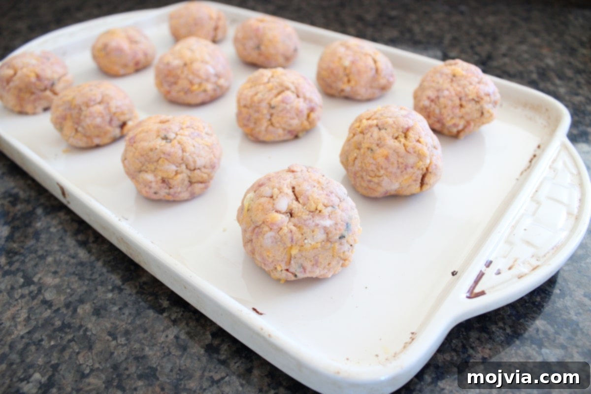 Several gluten-free sweet potato sausage balls, perfectly formed and arranged on a parchment-lined baking sheet, ready for the oven.