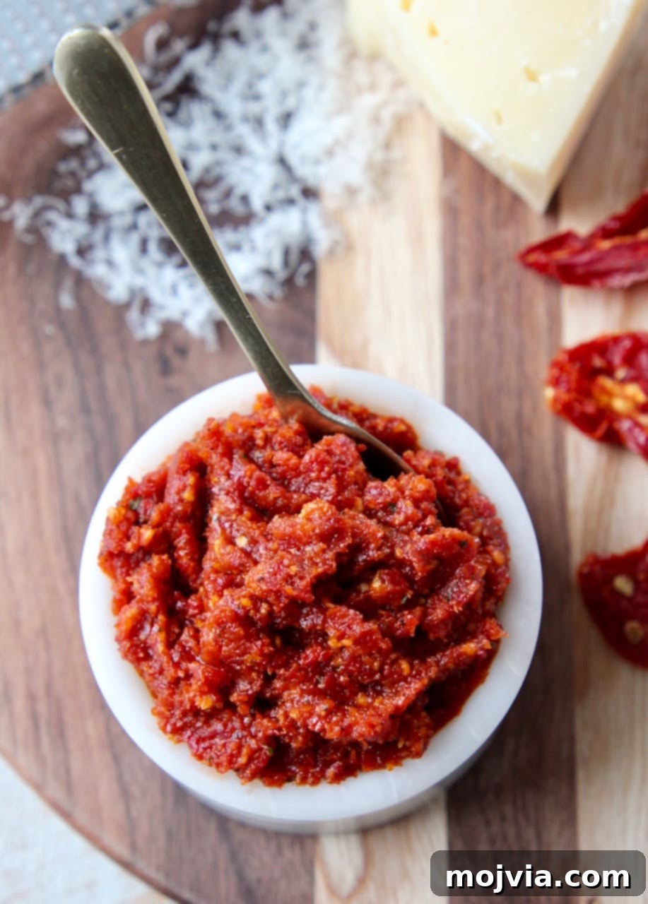 Vibrant sun-dried tomato pesto in a small white bowl with a golden spoon, surrounded by dried tomatoes