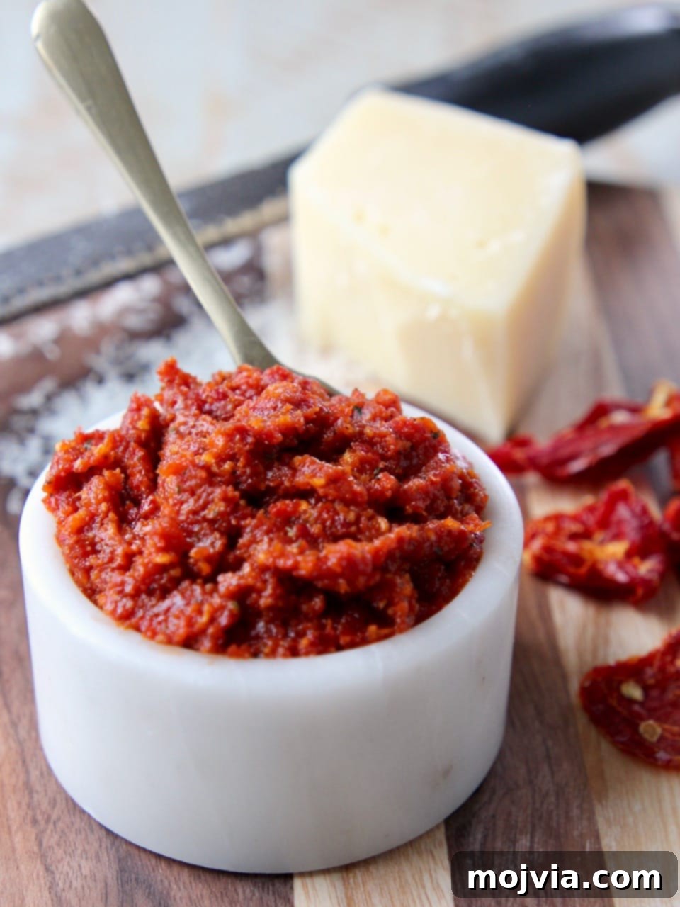 Sun-dried tomato pesto in a white bowl, with a block of Parmesan cheese in the background