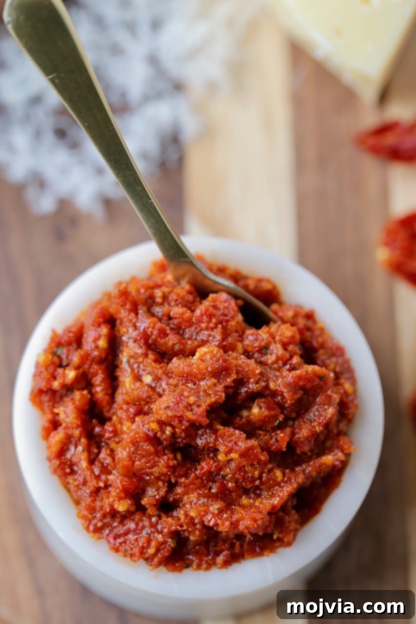 Sun Dried Tomato Pesto in a white bowl with a small gold spoon on a rustic wood cutting board
