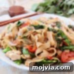 Drunken noodles with tomatoes and Chinese broccoli on white plate with chopsticks on the side