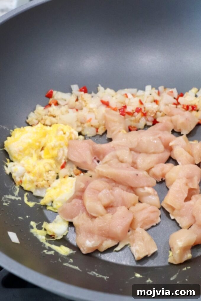 diced raw chicken in large wok with scrambled eggs and diced vegetables