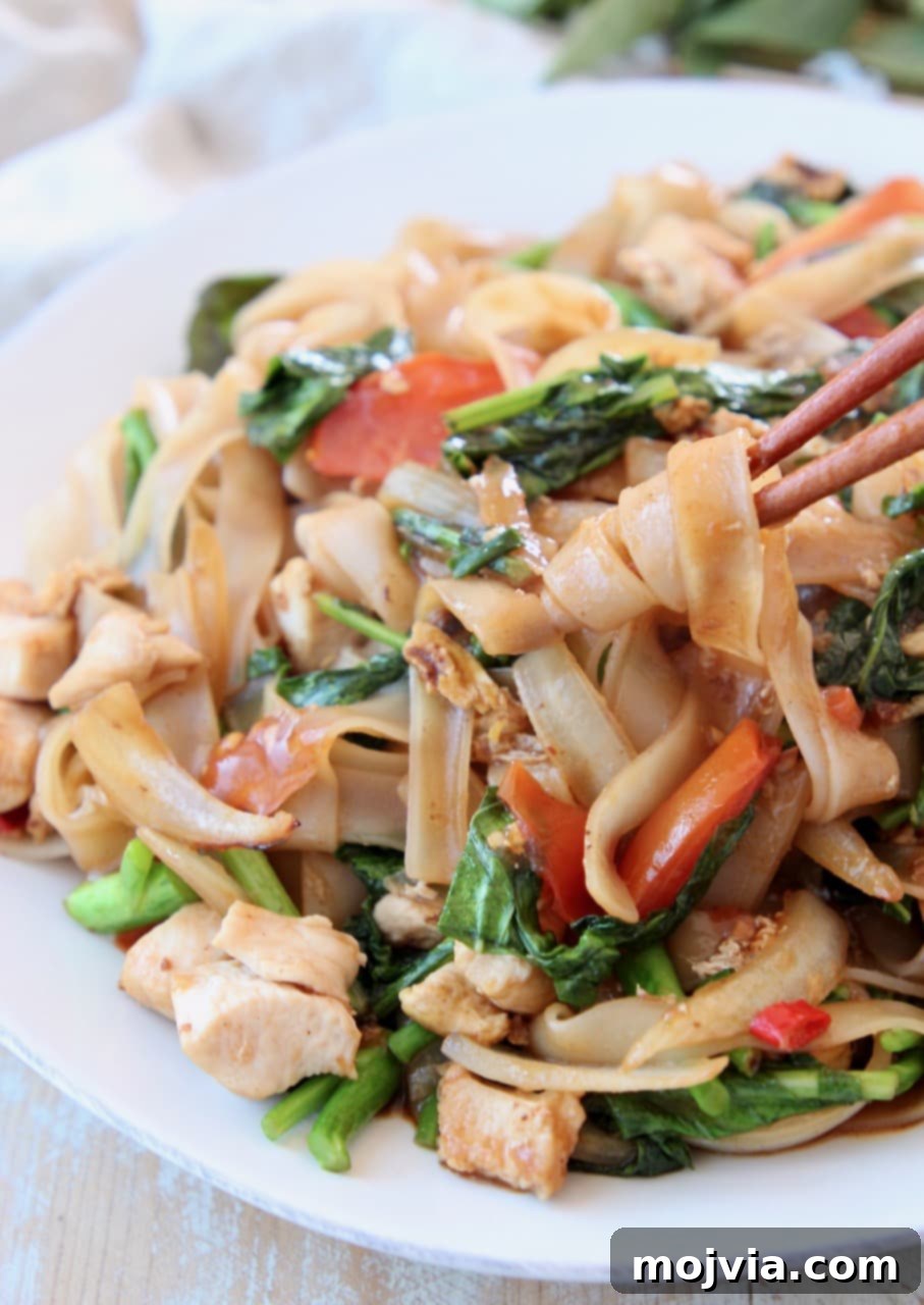 Drunken noodles, twirled around chopsticks on white plate
