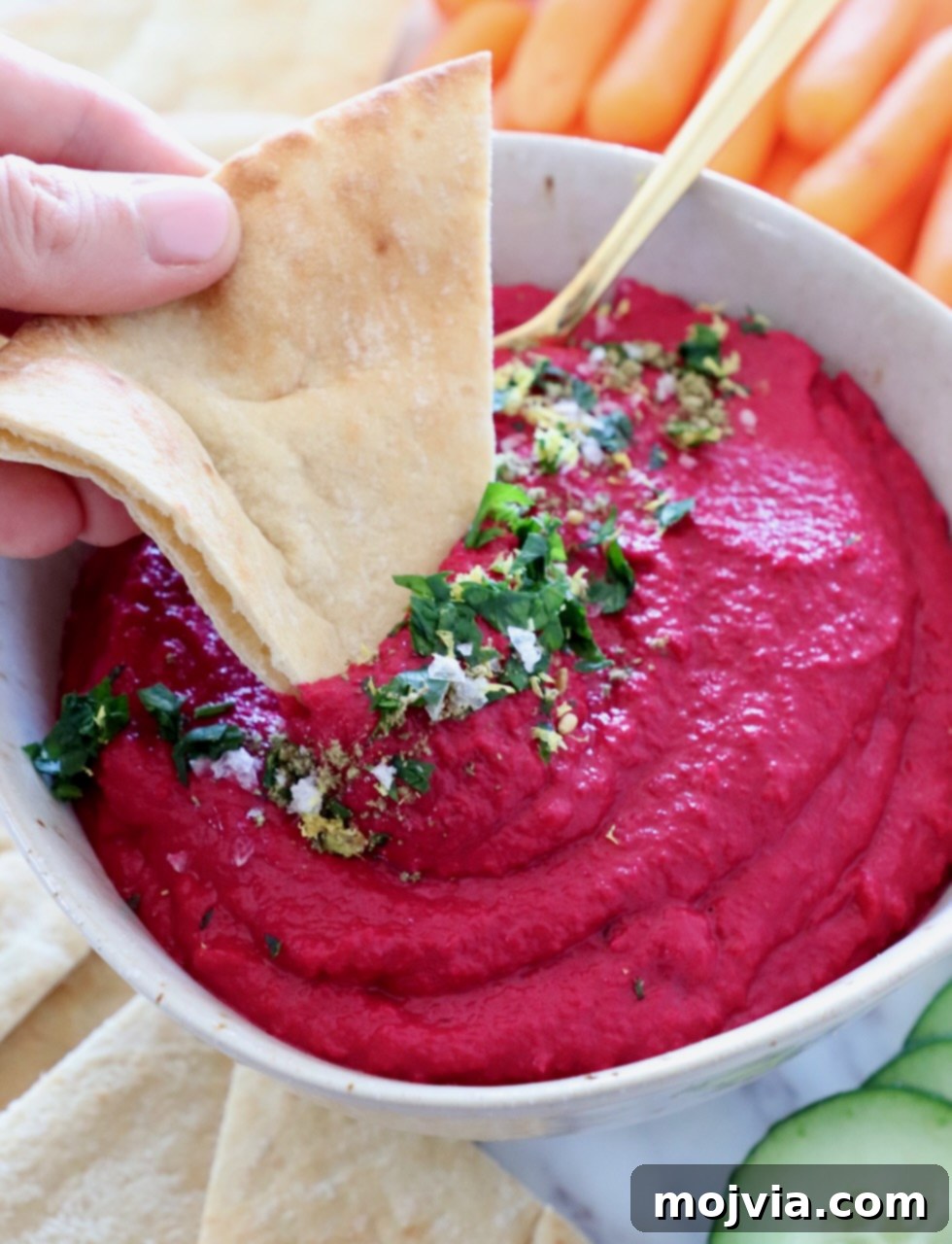 Blush Beet Hummus 11 A bowl of beet hummus with a piece of pita bread dipped in, highlighting the dip's appealing texture and color.
