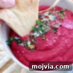 beet hummus in bowl with piece of pita bread dipped into the hummus