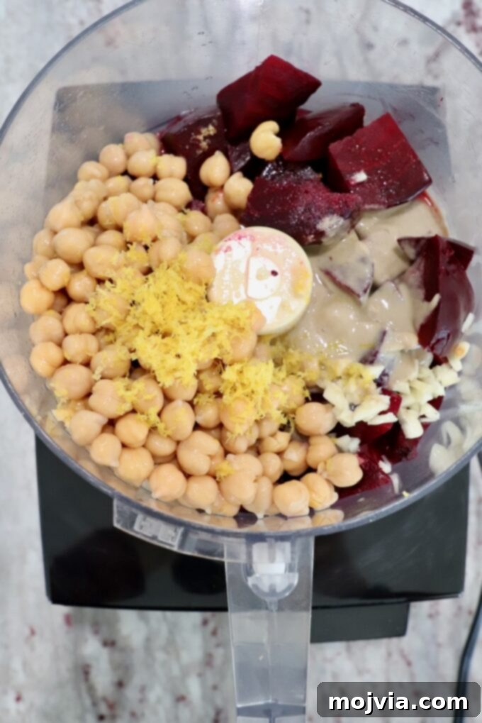 Blush Beet Hummus 8 All main ingredients for beet hummus, including beets, chickpeas, tahini, garlic, lemon zest and juice, and salt, added to a food processor.