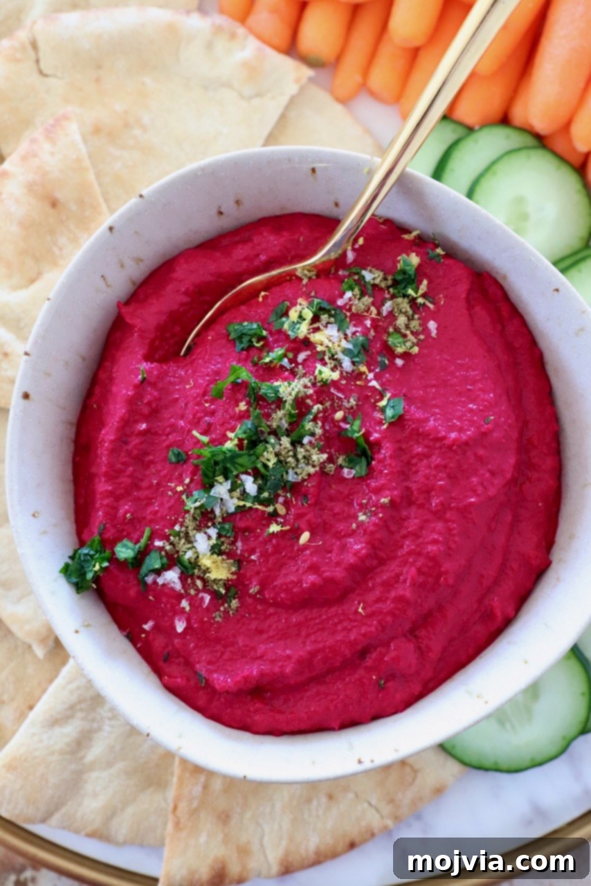 Blush Beet Hummus 10 A bowl of vibrant beet hummus with a golden spoon, garnished with fresh parsley and a drizzle of olive oil, ready to be served.