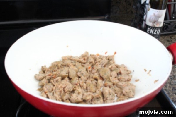 Sun-Drenched Sausage & Cheese Pasta Shells 6 Savory Italian chicken sausage cooking and crumbling in a vibrant red and white skillet, creating a delicious aroma.