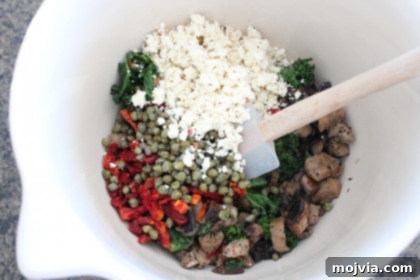 Sun-Drenched Sausage & Cheese Pasta Shells 8 A pristine white bowl filled with a colorful and aromatic mixture of sausage, onion, kale, capers, sun-dried tomatoes, and crumbled feta cheese, ready for stuffing.