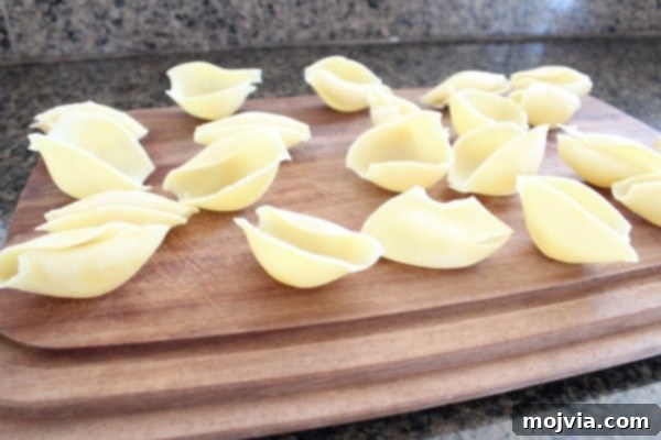 Sun-Drenched Sausage & Cheese Pasta Shells 9 Perfectly cooked jumbo pasta shells laid out neatly on a rustic wooden cutting board, cooling and ready to be stuffed.