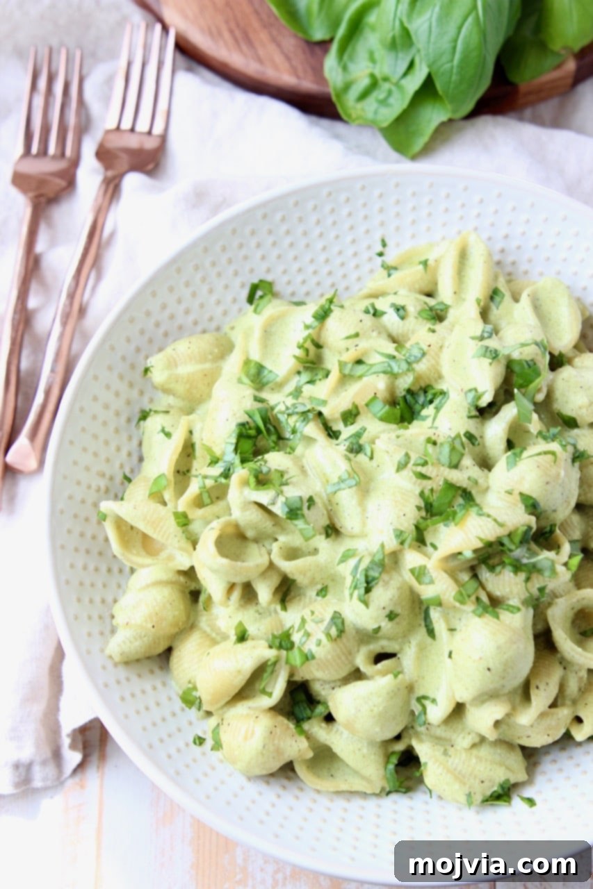 Vibrant Basil Pesto Pasta with Gooey Cheese 4 Overhead shot of cheesy basil pesto pasta in white bowl with copper forks on the side