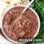 Fresh tomato salsa in a bowl with a spoon, highlighting its chunky texture and vibrant color.