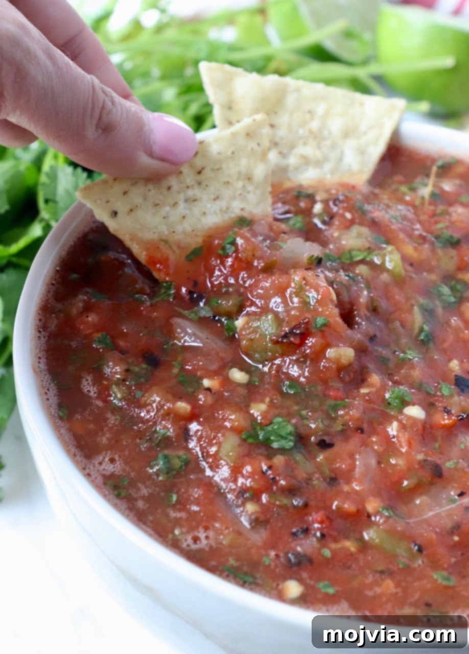 Your Go-To 10-Minute Fresh Salsa 6 A hand dipping a crispy tortilla chip into a bowl of freshly made, chunky tomato salsa, showcasing its perfect texture.