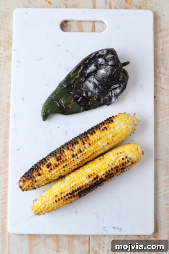 Fiesta Corn Salsa 4 Grilled corn on the cob and a charred poblano pepper resting on a cutting board, ready for preparation into salsa.