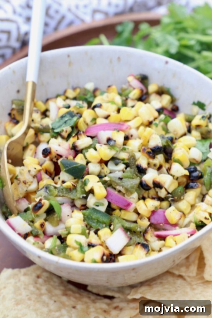 Fiesta Corn Salsa 5 A bowl of fresh corn salsa with a spoon, garnished with cilantro, ready to be enjoyed.