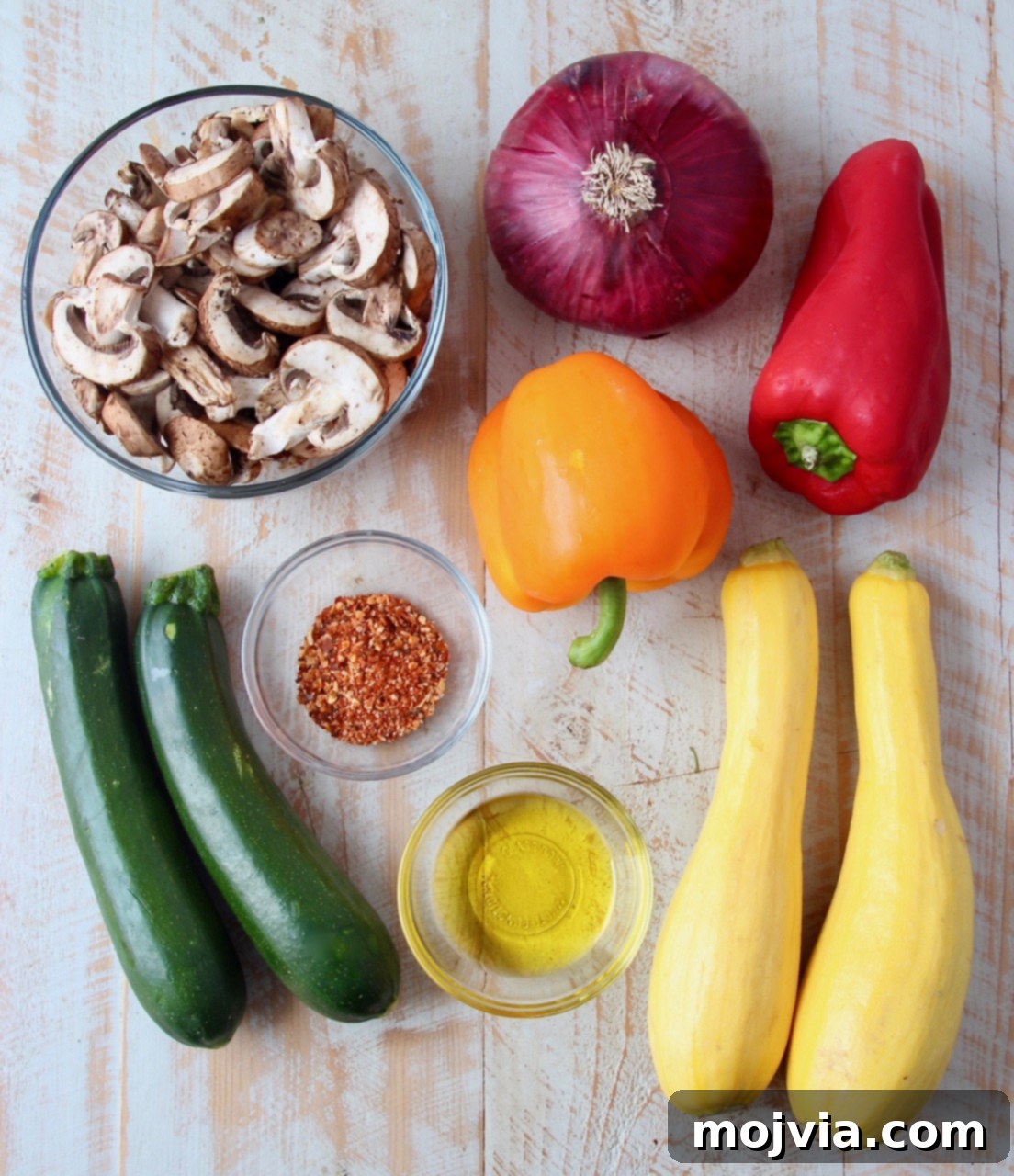 Vibrant Grilled Vegetable Skewers 3 A selection of fresh vegetables including baby bella mushrooms, bell peppers, zucchini, yellow summer squash, and red onion, laid out on a white wooden board, ready for grilling.