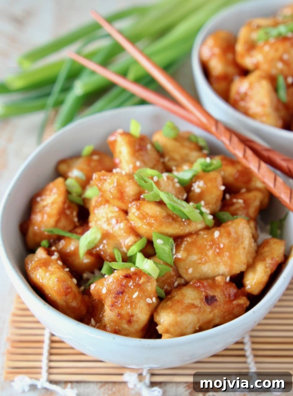 Zesty Gluten-Free Orange Chicken 11 Orange chicken in bowl topped with sliced scallions and sesame seeds, with wooden chopsticks resting on the side