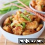 Gluten-Free Orange Chicken in a bowl with scallions and wooden chopsticks
