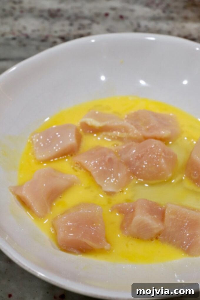 Zesty Gluten-Free Orange Chicken 5 Pieces of chicken being dipped in whisked egg