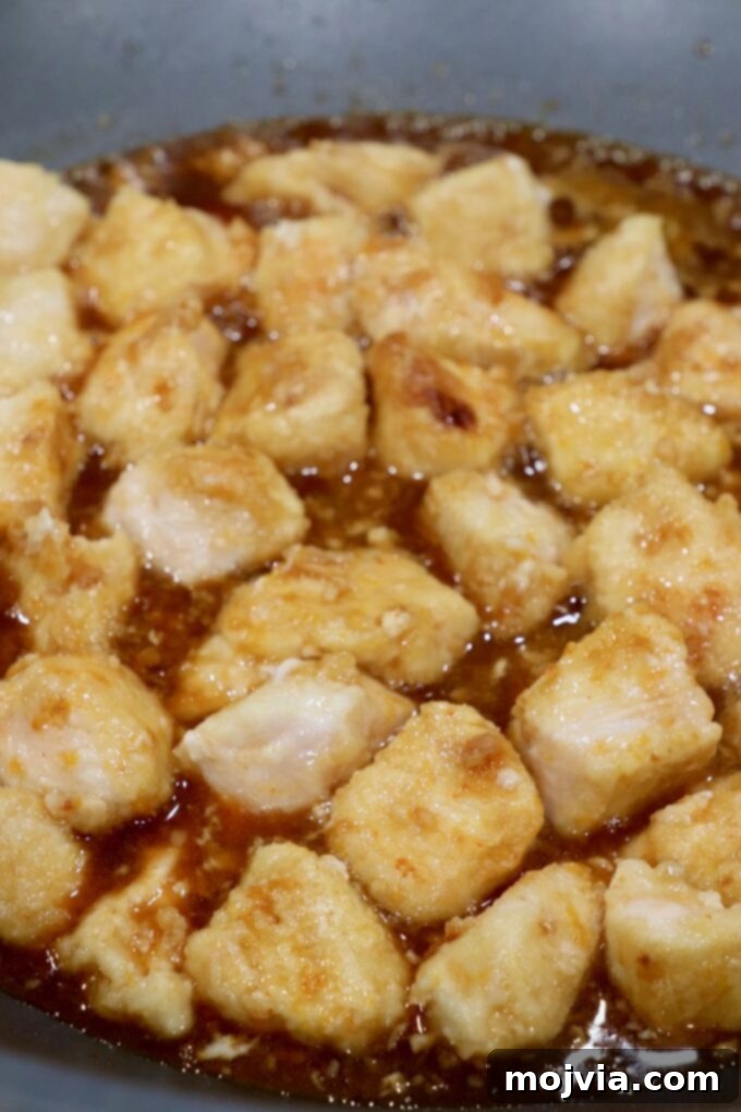 Zesty Gluten-Free Orange Chicken 8 Cooked chicken pieces immersed in orange sauce in a skillet