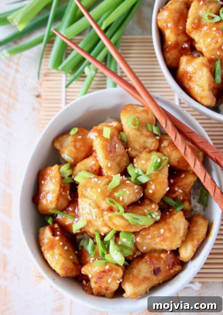 Zesty Gluten-Free Orange Chicken 10 Orange chicken in bowl with diced scallions and wooden chopsticks, ready to be served
