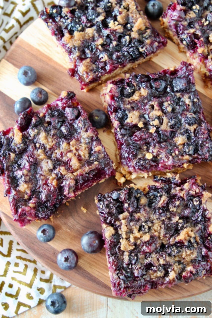 Gluten-Free Blueberry Bliss Bars 5 Close-up shot of gluten-free blueberry oat bars, perfectly sliced into squares and arranged on a wooden cutting board with a sprinkling of fresh blueberries.