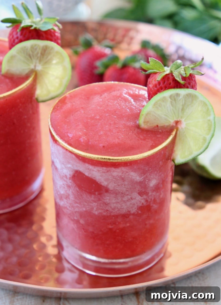 Basil Infused Strawberry Daiquiri 2 Vibrant frozen strawberry daiquiri in a stemmed glass, garnished with a lime wedge and a fresh strawberry on the rim, evoking a sense of tropical relaxation.
