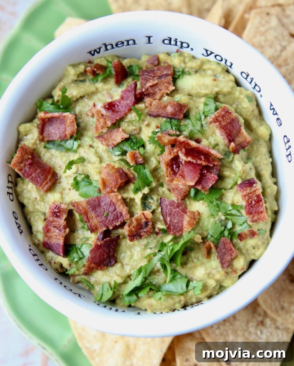 Smoky Chipotle Bacon Guac 2 Creamy Chipotle Bacon Guacamole in a white bowl, generously topped with crumbled cooked bacon, ready for dipping.