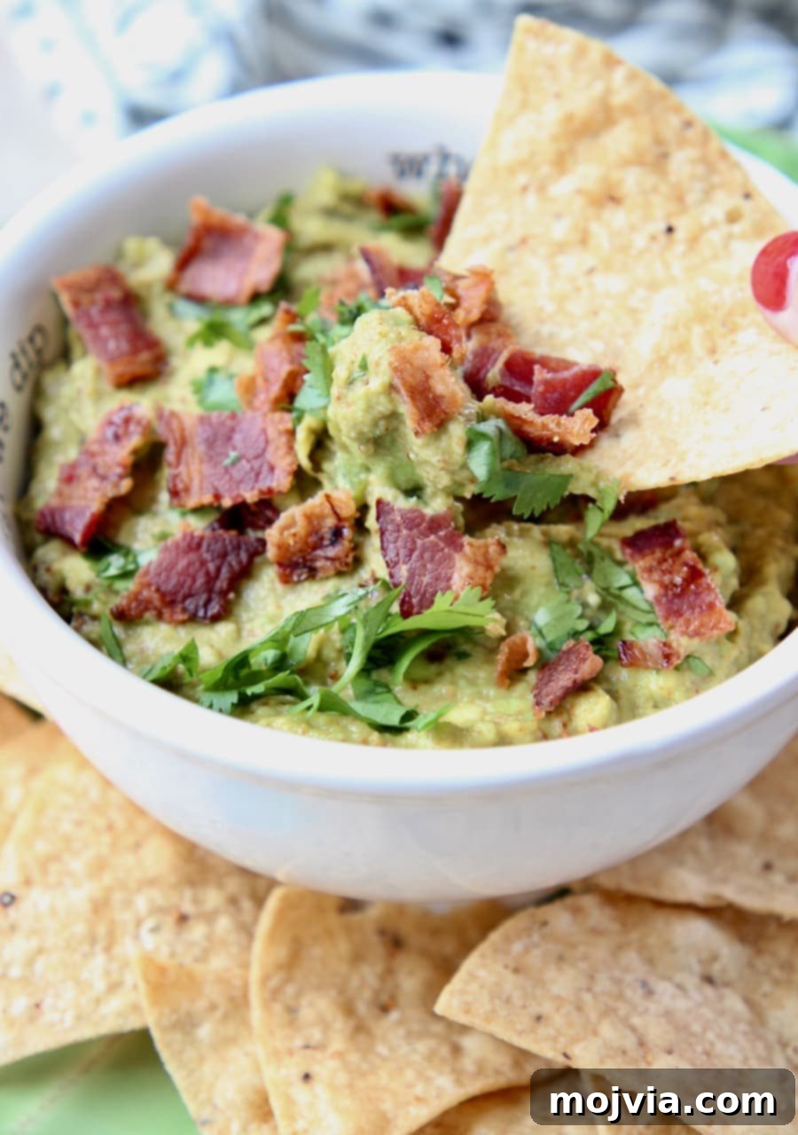 Smoky Chipotle Bacon Guac 3 Crispy tortilla chip perfectly dipped into a bowl of Chipotle Bacon Guacamole, showing off its creamy texture and bacon bits.