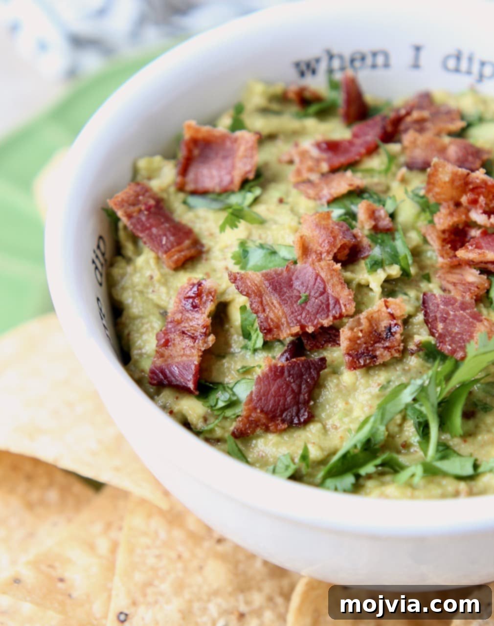 Smoky Chipotle Bacon Guac 4 A beautifully presented bowl of Chipotle Bacon Guacamole, garnished with fresh cilantro and extra bacon bits, ready to be enjoyed.