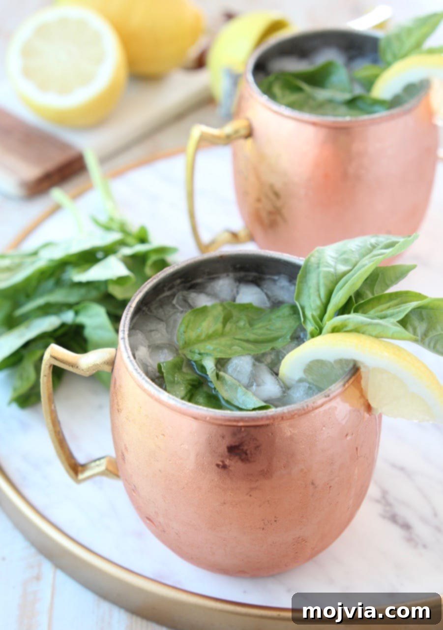 Sun-Kissed Peach Basil Mule 2 Moscow mule in copper mugs with fresh basil and lemon wedge on the side, on a rustic wooden surface