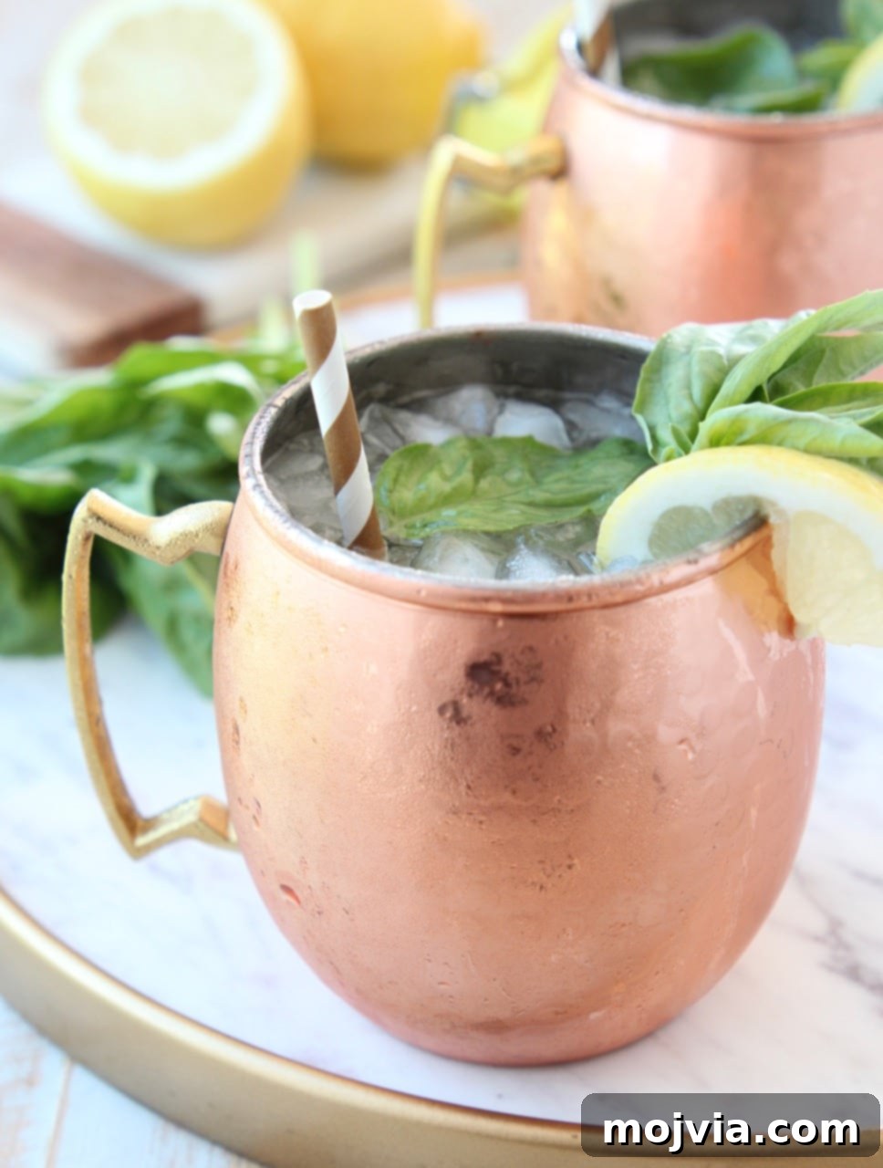 Sun-Kissed Peach Basil Mule 3 Copper mug filled with vodka, ice, ginger beer, fresh lemon and basil, on a white marble surface