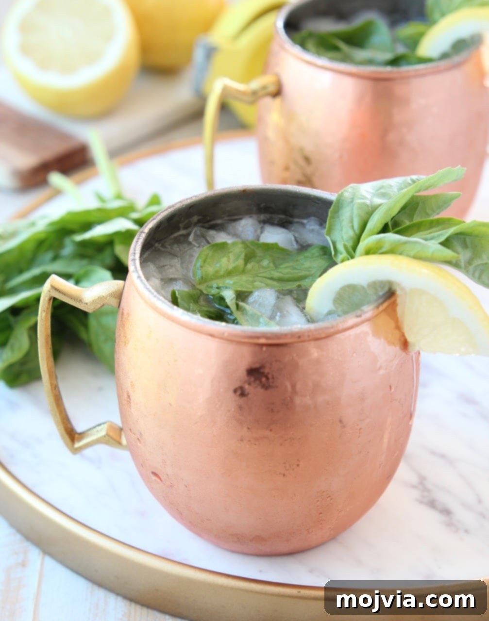 Sun-Kissed Peach Basil Mule 4 Copper mug filled with ice, vodka and ginger beer, on marble tray with lemon and basil garnish