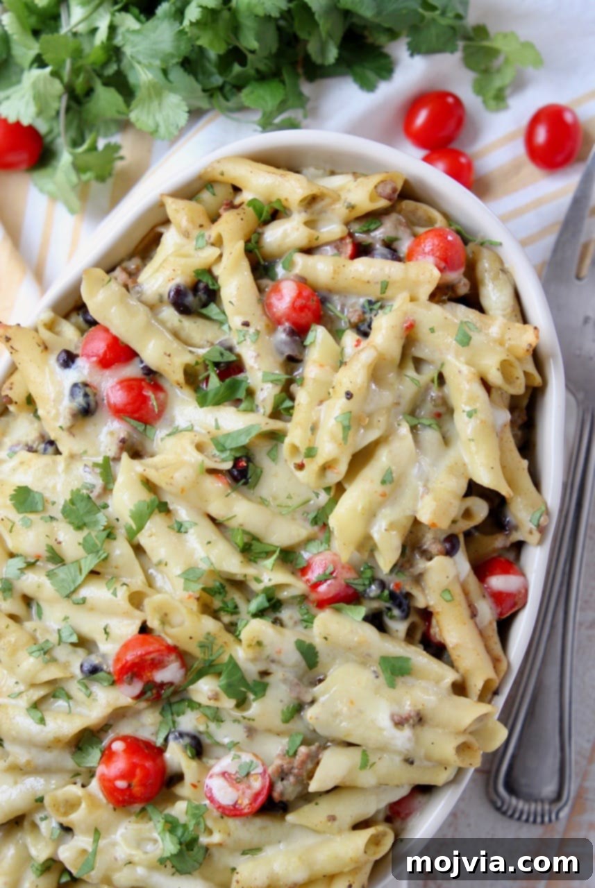 Zesty Taco Pasta Bake with Avocado Cream 3 Close-up of baked taco pasta in a casserole dish, featuring black beans, cherry tomatoes, and fresh cilantro garnish