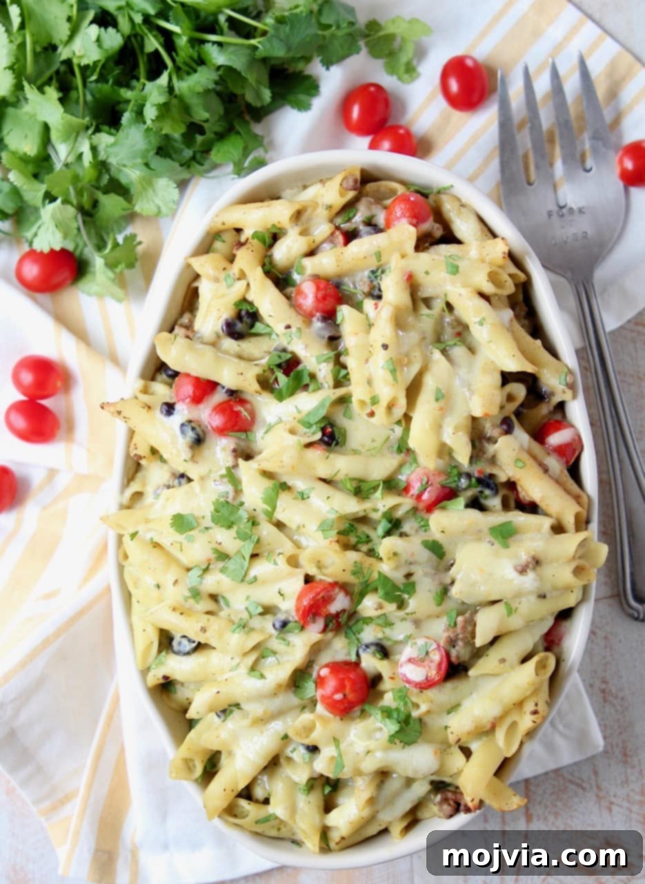 Zesty Taco Pasta Bake with Avocado Cream 4 Taco pasta in large oval casserole dish with a serving fork, garnished with cherry tomatoes on the side