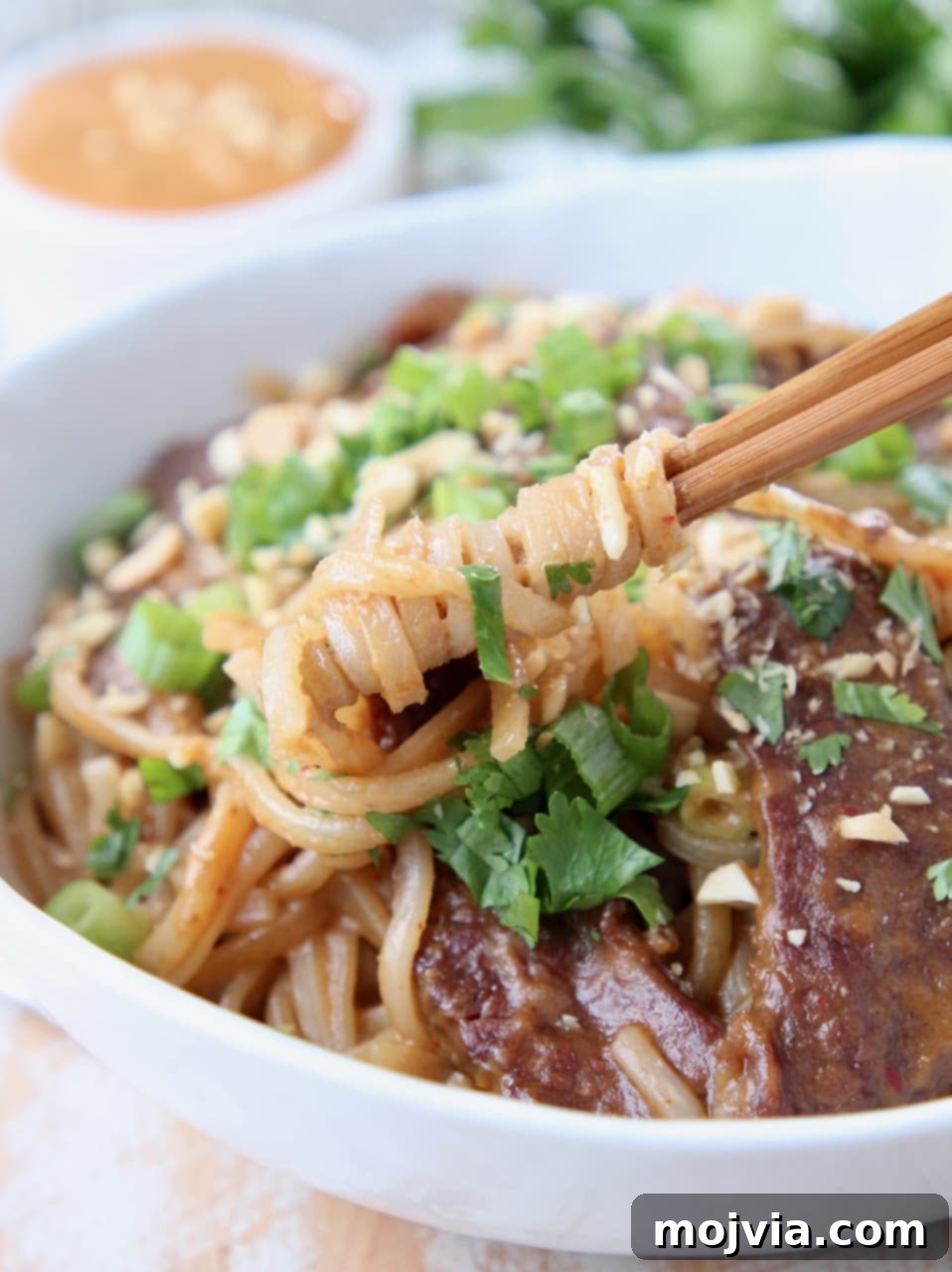 Bangkok Street Beef Noodles 3 Close-up of perfectly cooked rice noodles swirled around chopsticks in a Thai beef noodle bowl, garnished with fresh cilantro and crunchy chopped peanuts.