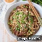 Overhead shot of sliced beef and noodles in a white bowl with chopsticks on the side, ready to eat.