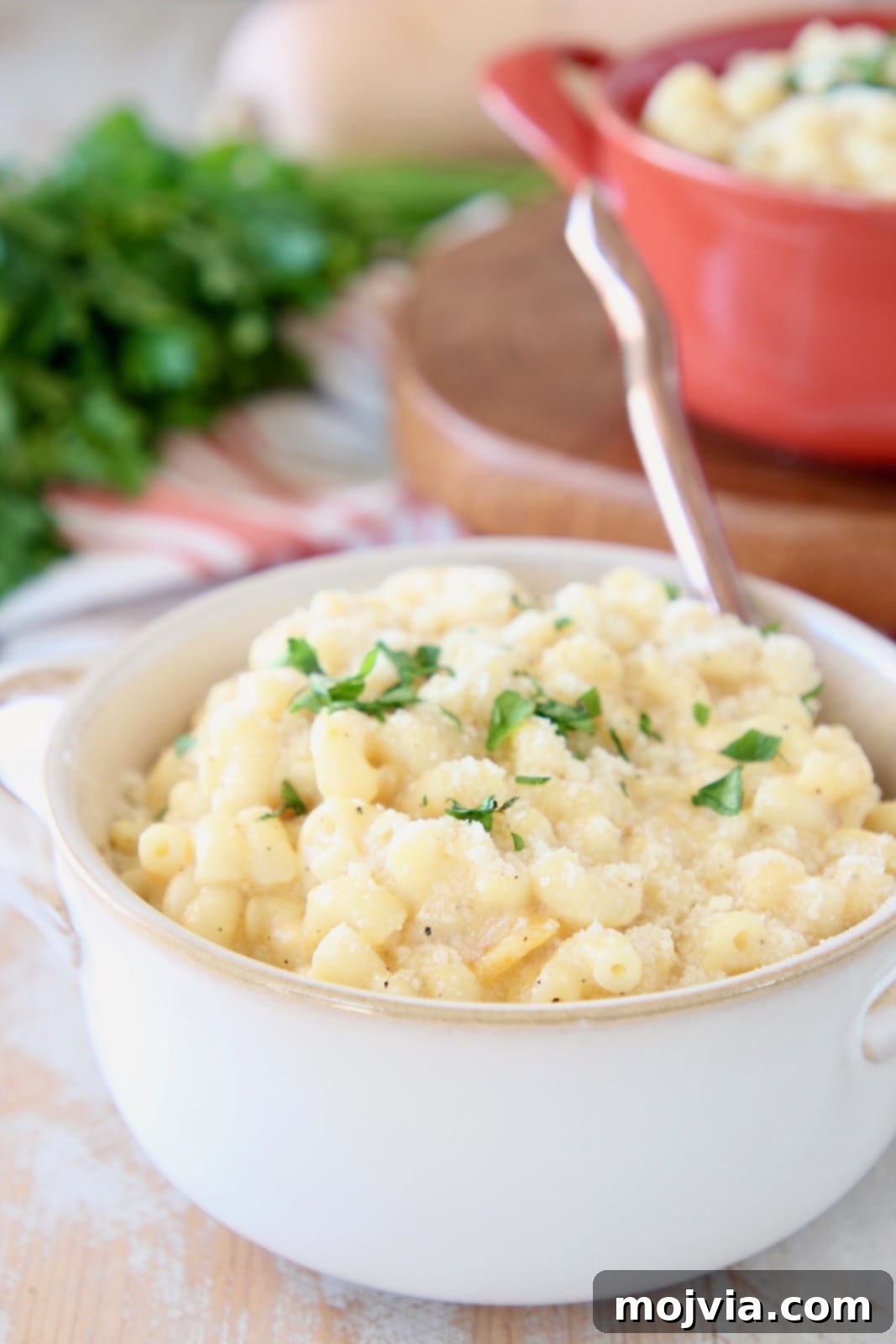 Butternut Squash Mac and Cheese in white crock with gold spoon and fresh chopped parsley